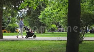 可爱的苗条妈妈带着婴儿车和她的小女儿在图片城公园的绿树中散步